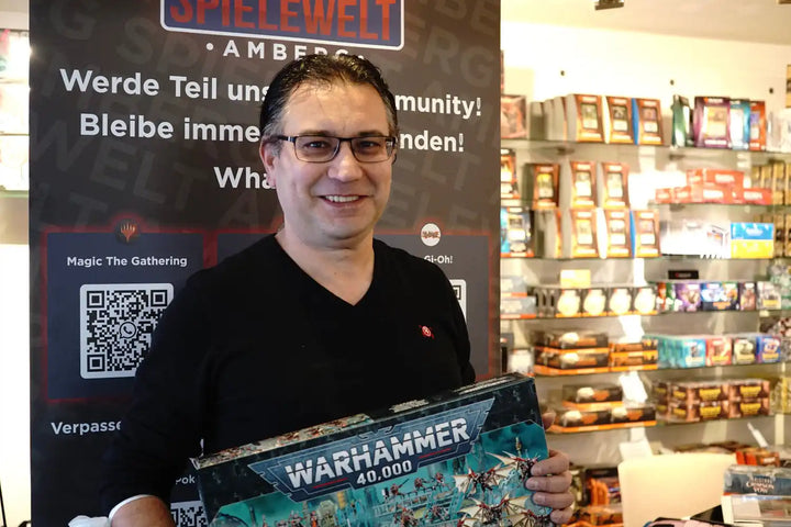 Jemand hält eine Warhammer-Spieleschachtel in einem, was wie ein Spieleladen aussieht.